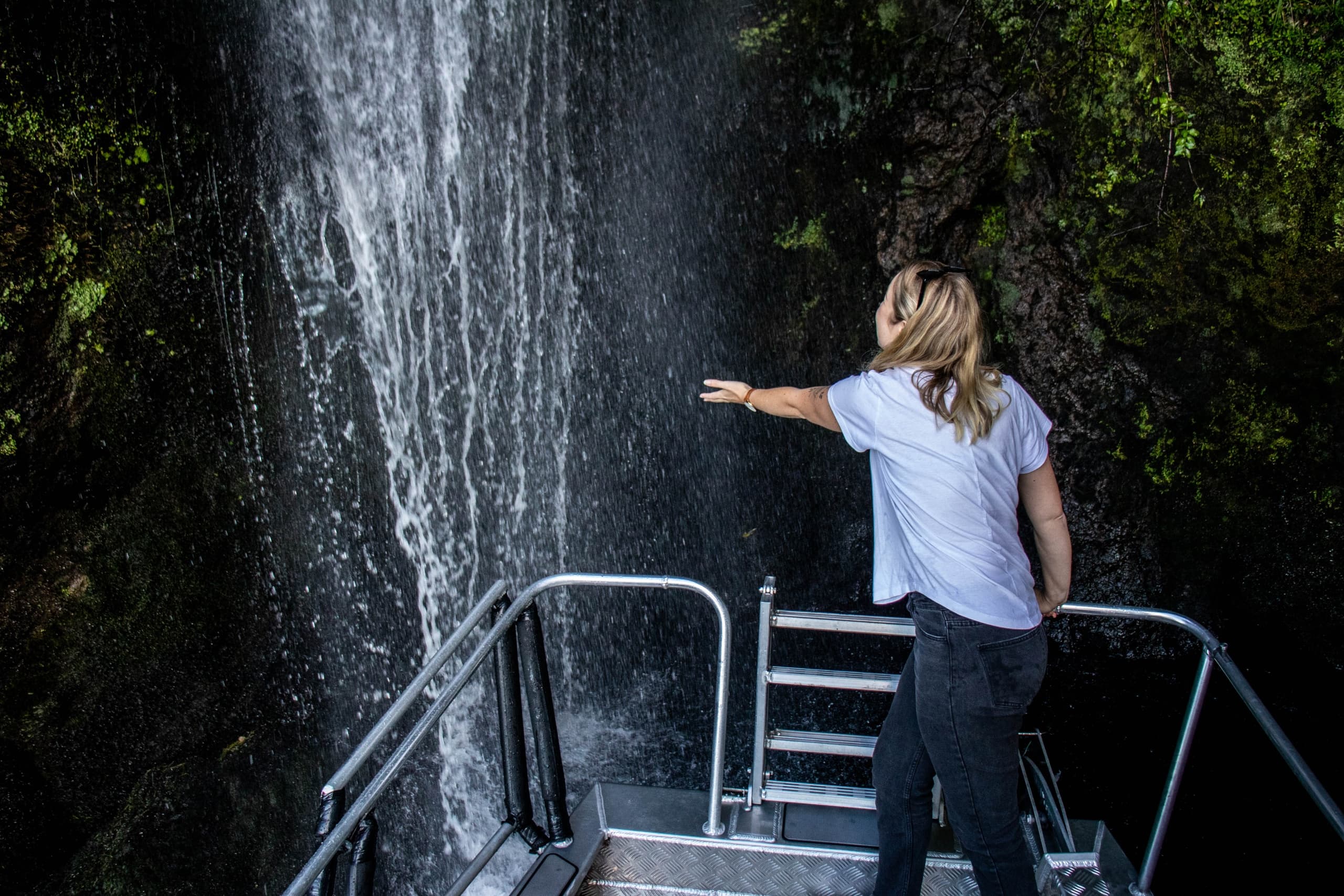 Visitor touching waterfall from viewing platform on coastal boat tour