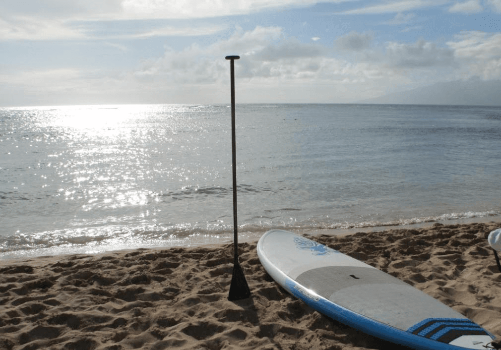 SUP paddleboard on sandy beach at calm sunrise lake