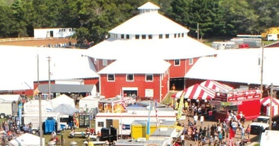 County fairgrounds with red barn, carnival tents, crowds