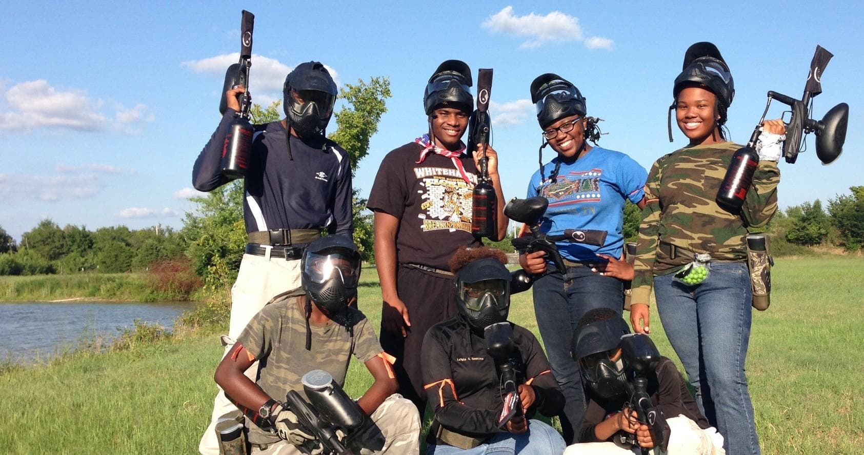 Paintball players posing with masks in grassy field