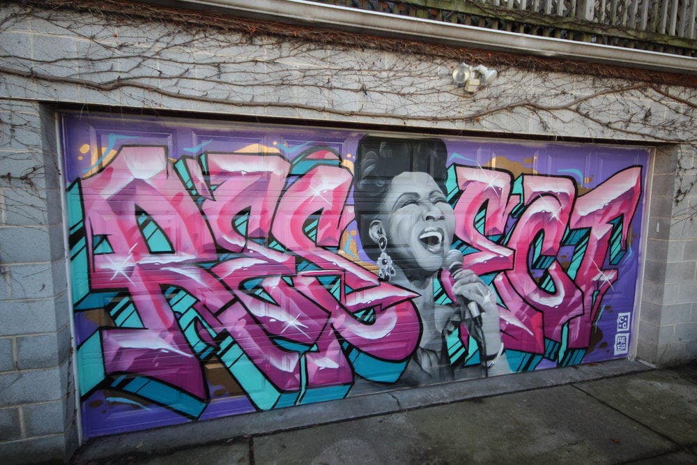 Garage-door graffiti portrait with vibrant lettering in alley