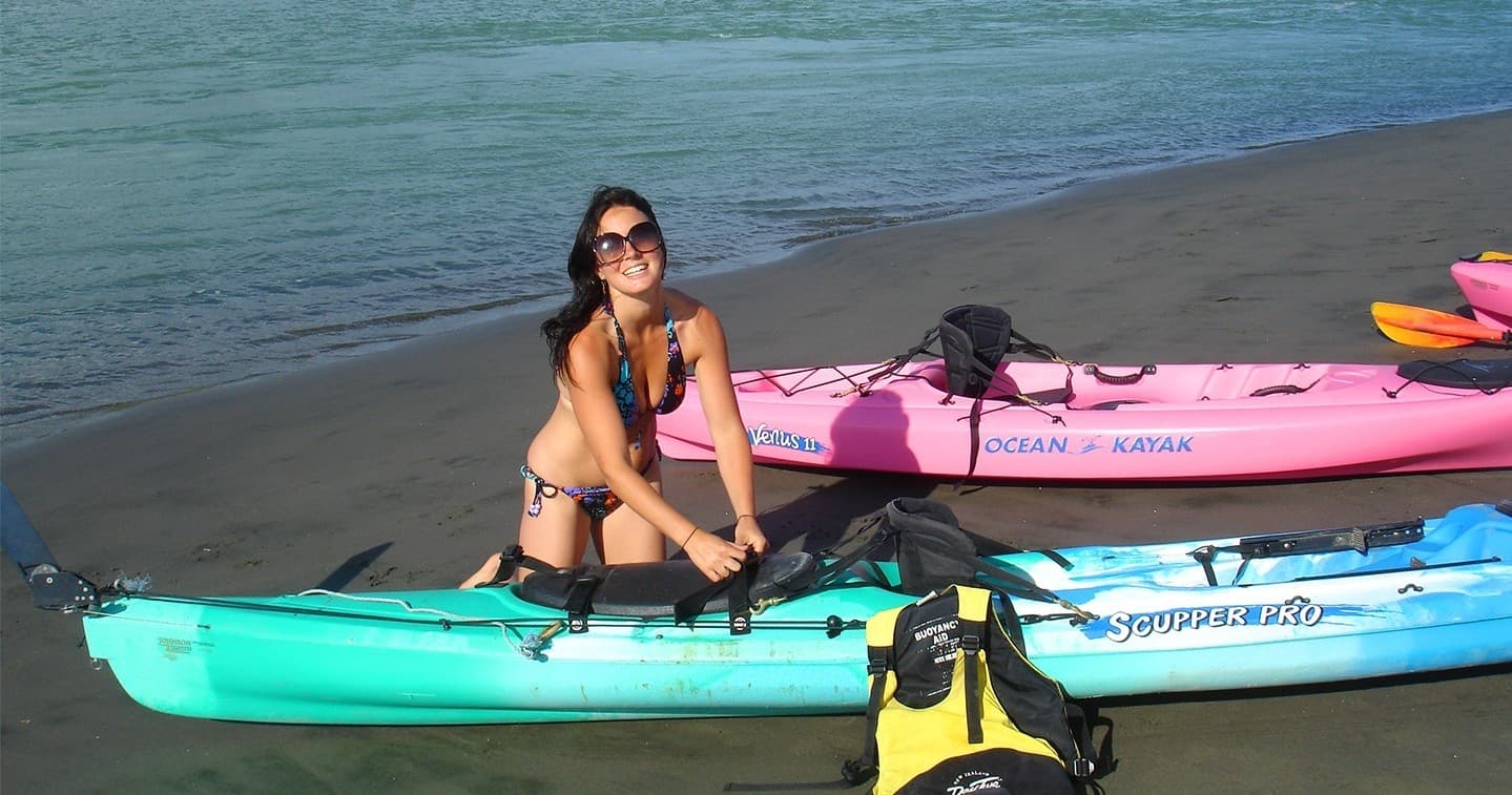 Woman preparing sit-on-top kayaks on sandy beach by calm sea