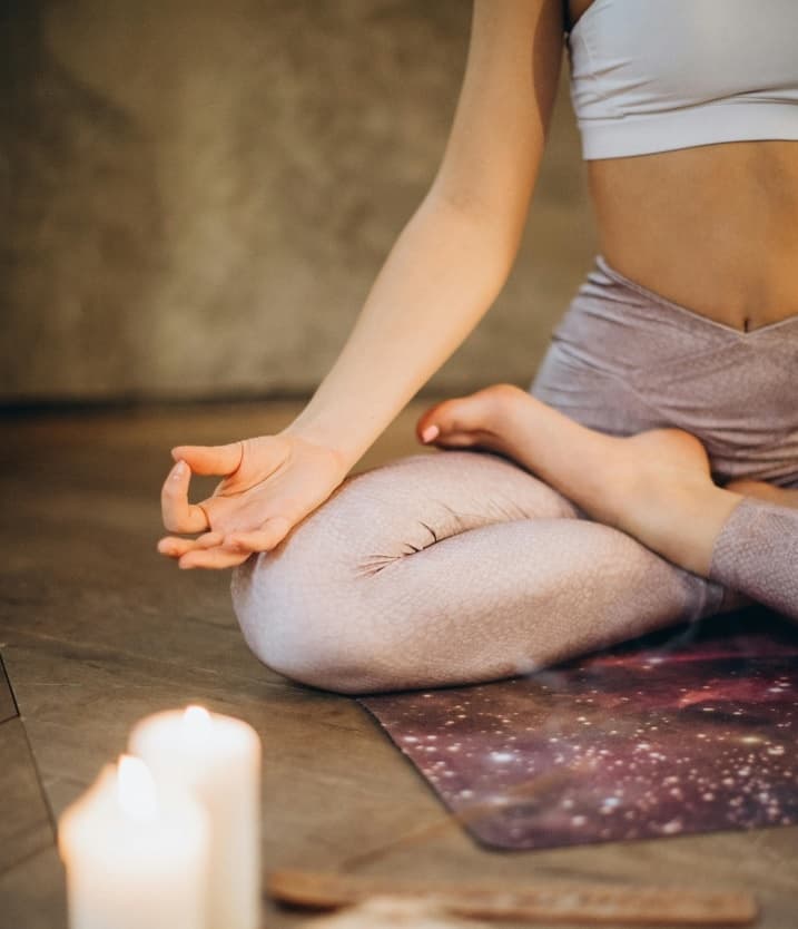 Person meditating on yoga mat with candles in indoor studio