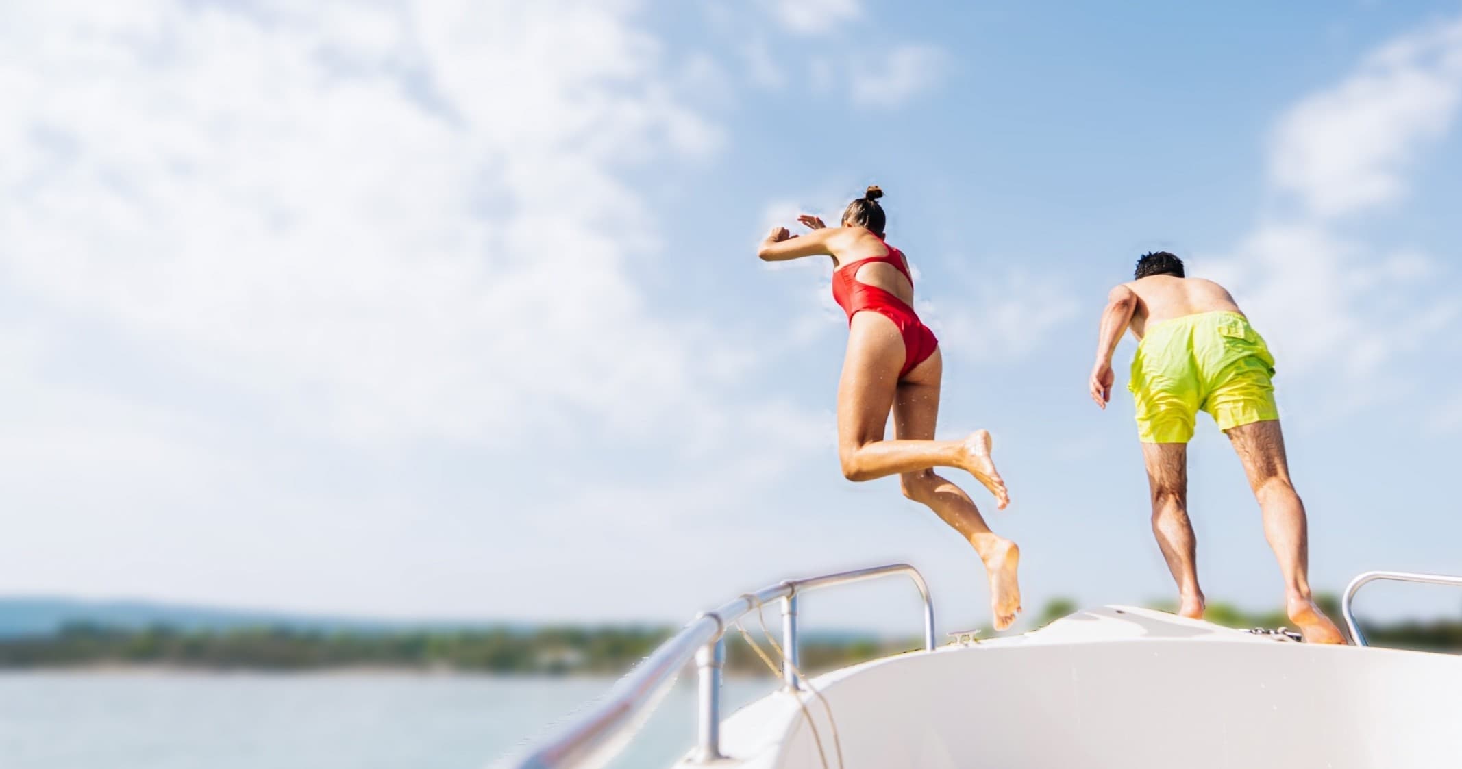 Couple jumping off boat into clear lake for summer boating fun