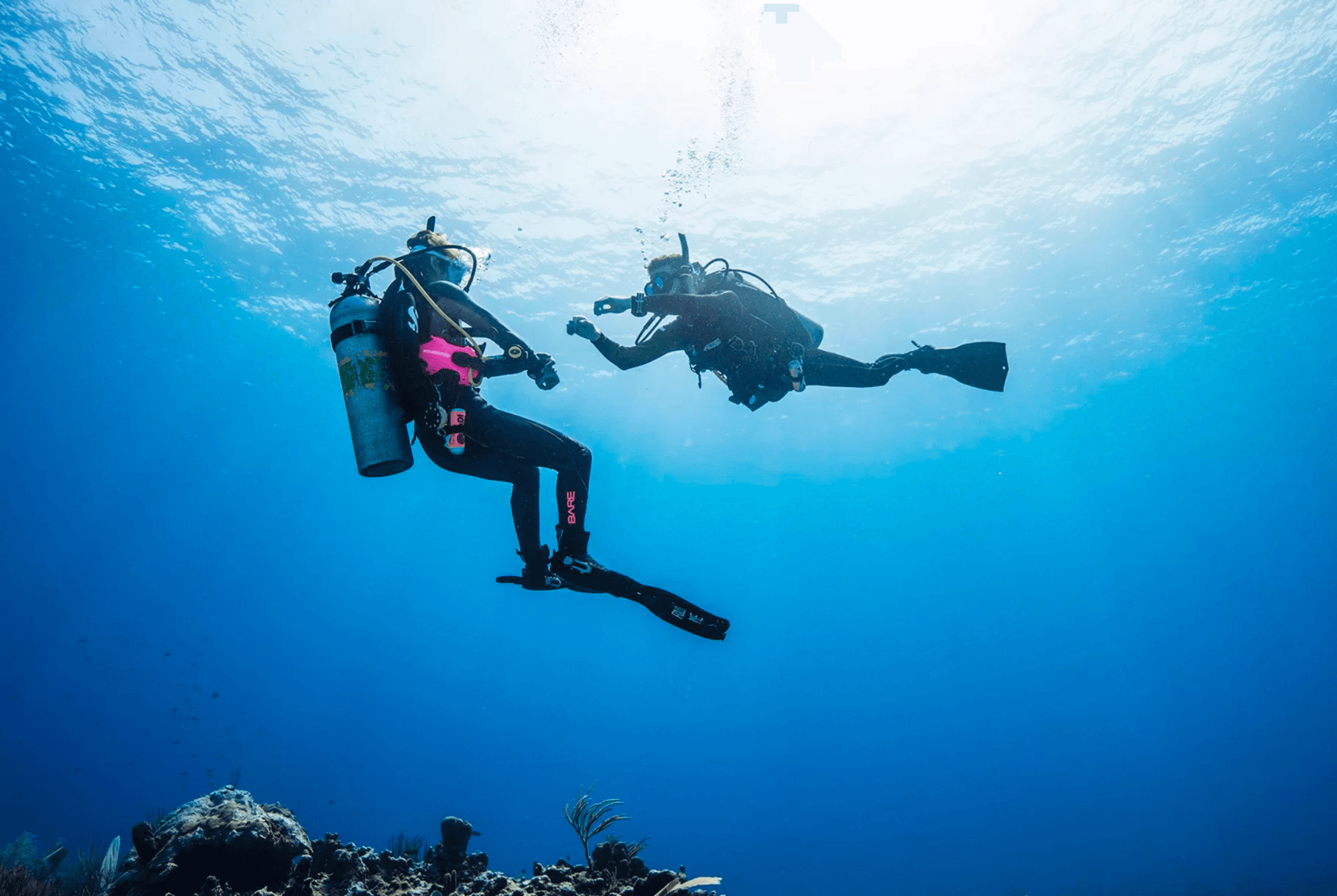 Two scuba divers ascending toward sunlit surface in open sea