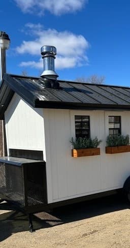 Mobile wood-fired sauna trailer parked outdoors for warming