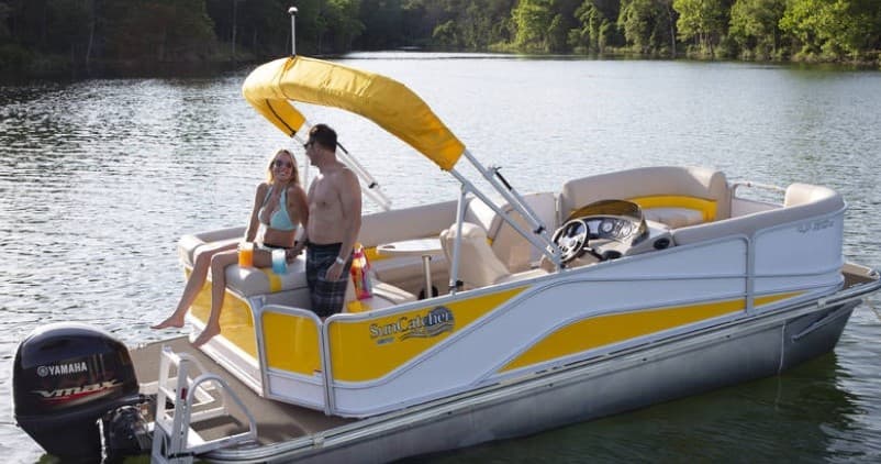 Couple relaxing on yellow pontoon boat cruising calm forested lake