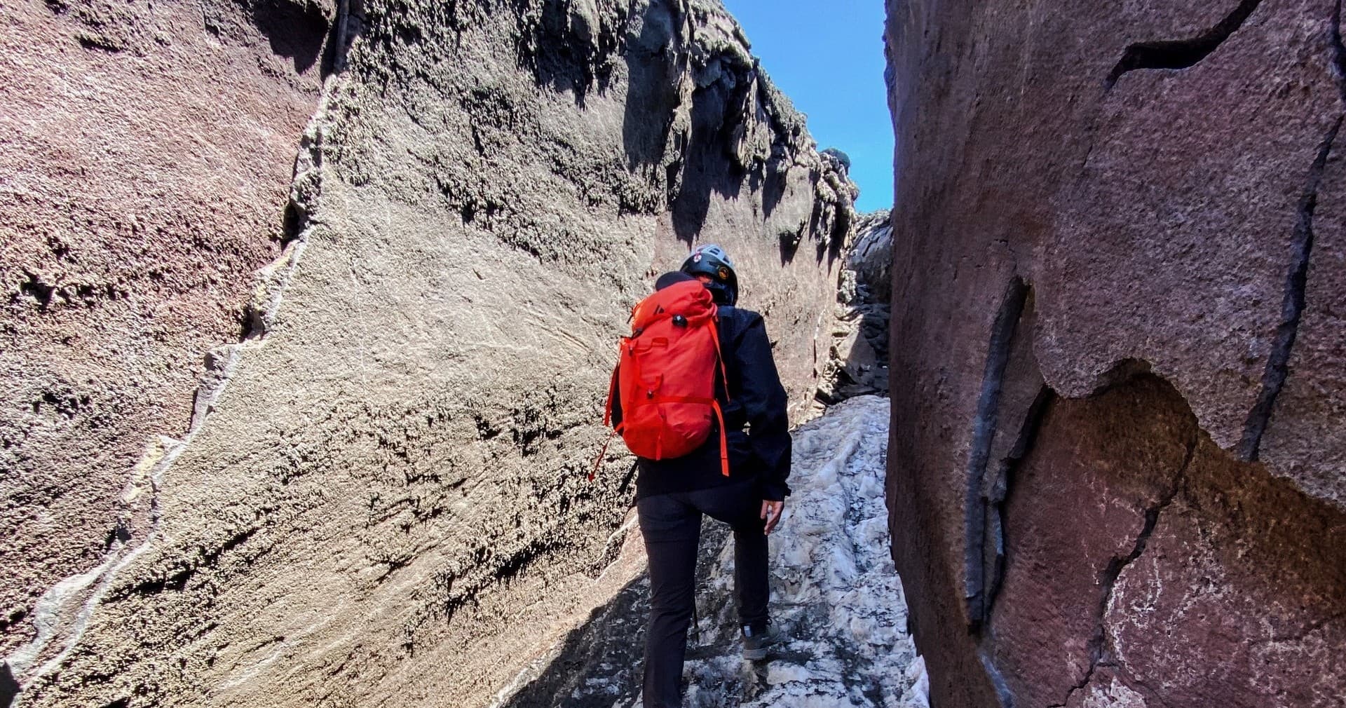 Trekkers hiking narrow volcanic canyon on Mount Etna with red pack
