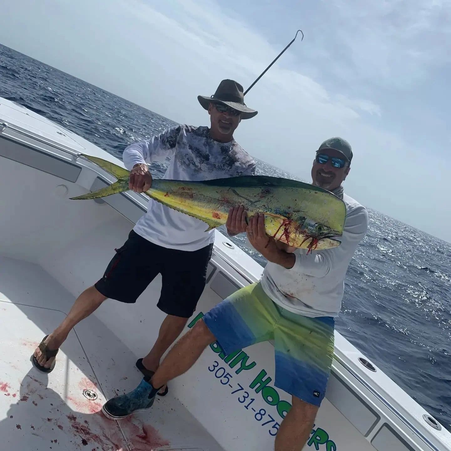 Two anglers holding large mahi-mahi aboard offshore fishing boat