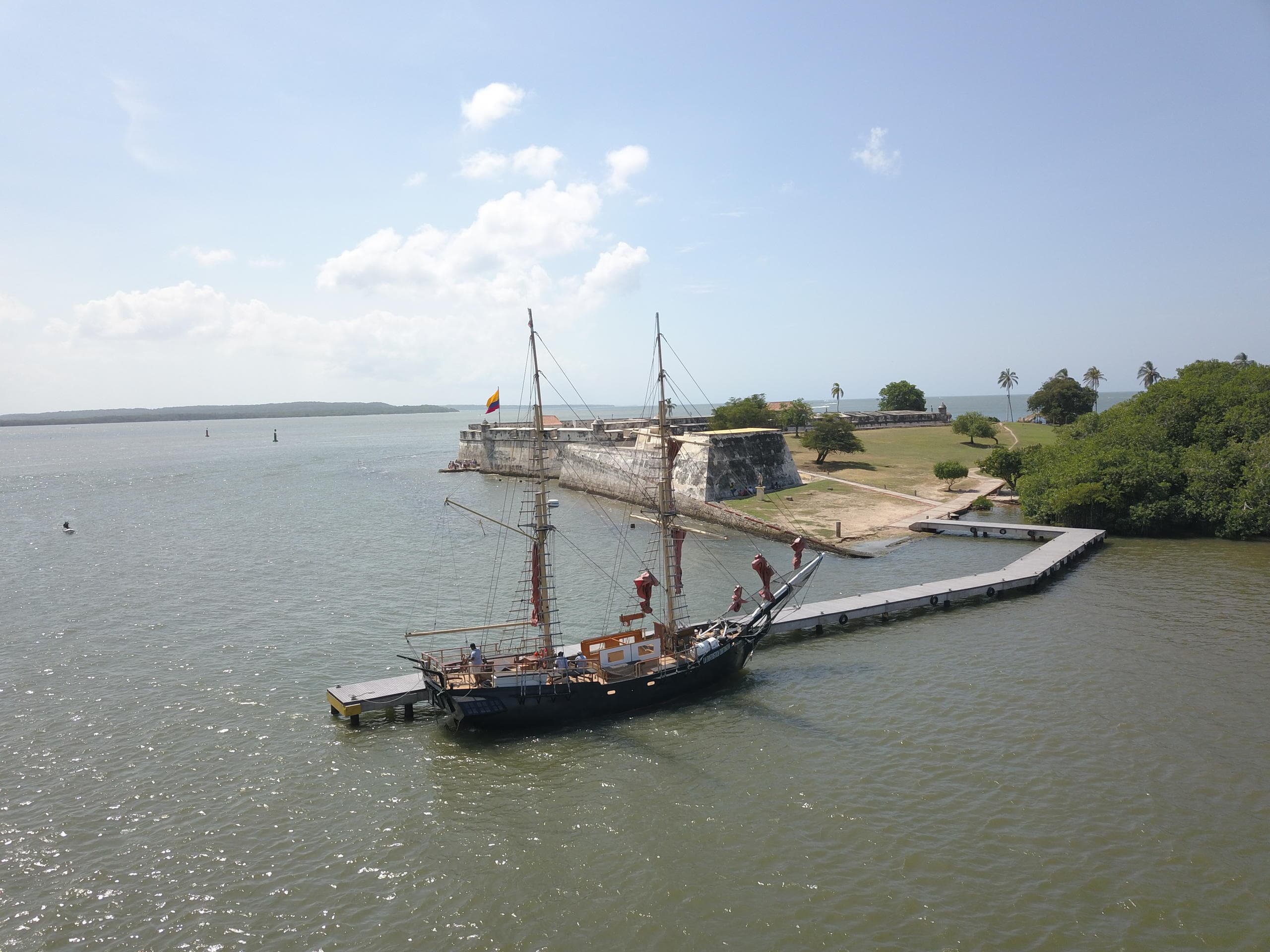 Historic ship moored by Cartagena fort and shoreline on sunny day
