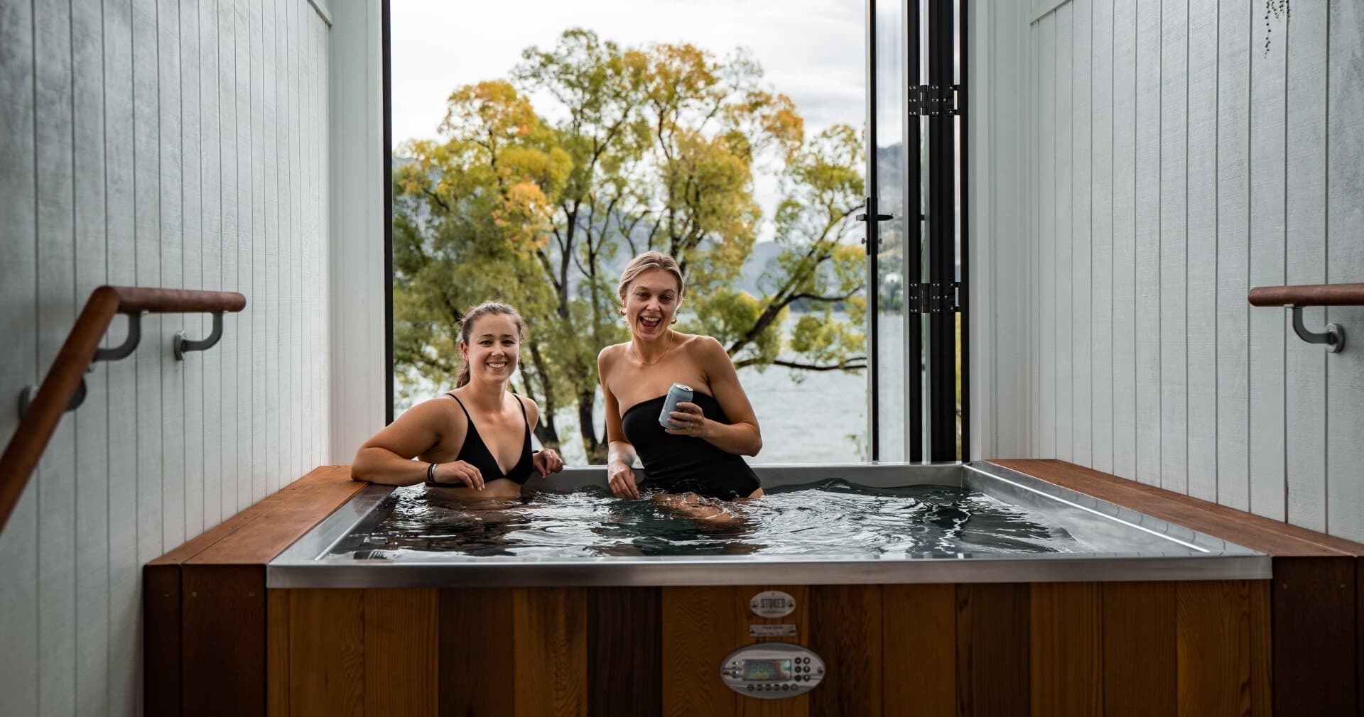 Two women relaxing in outdoor hot tub overlooking lake and trees