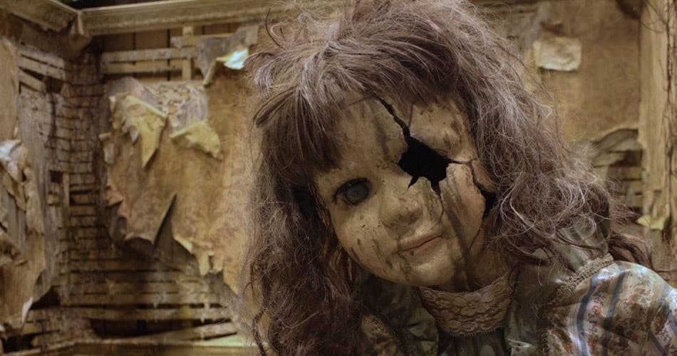 Creepy cracked doll in decayed indoor set of haunted mansion attraction