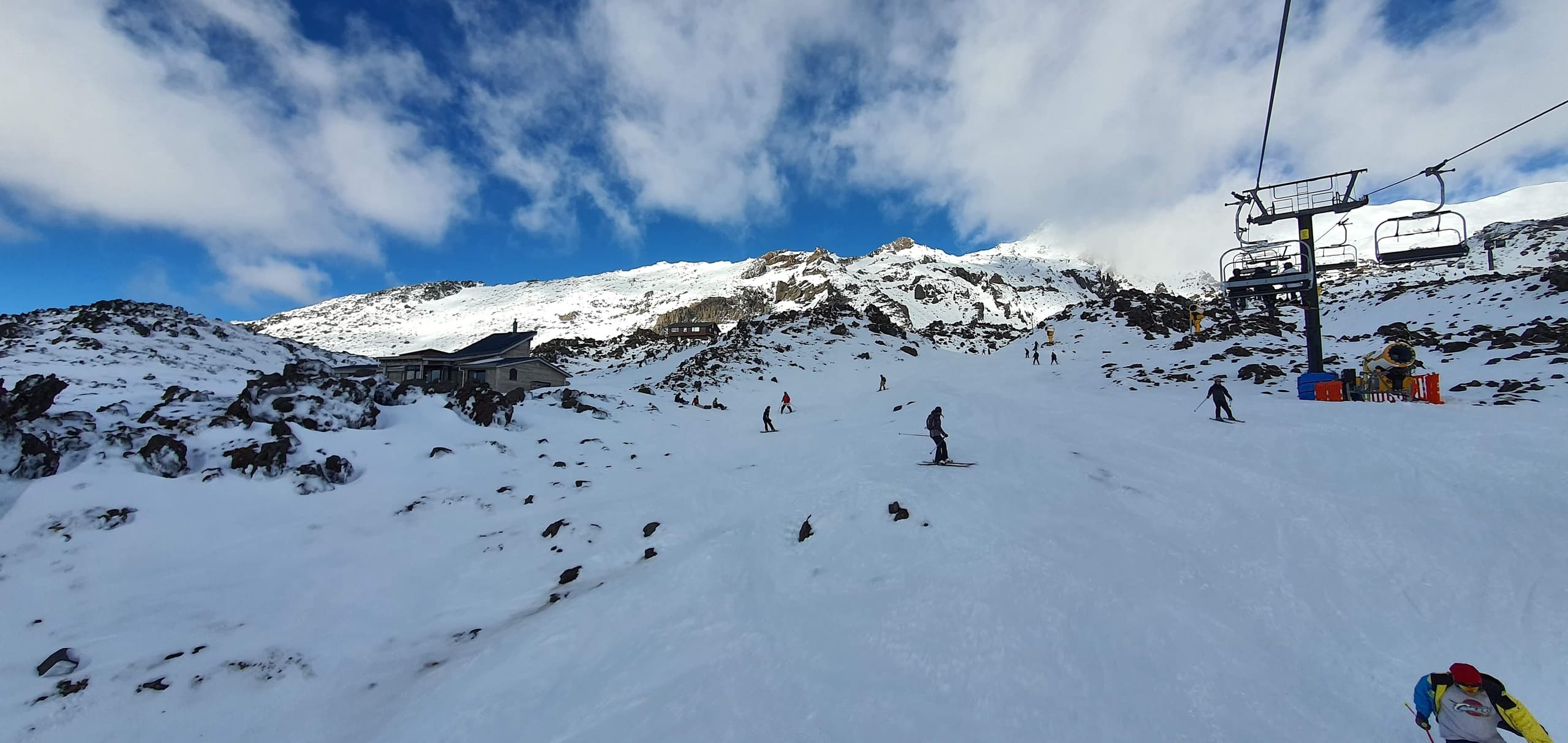 Skiers on snowy alpine slope with chairlift under blue sky