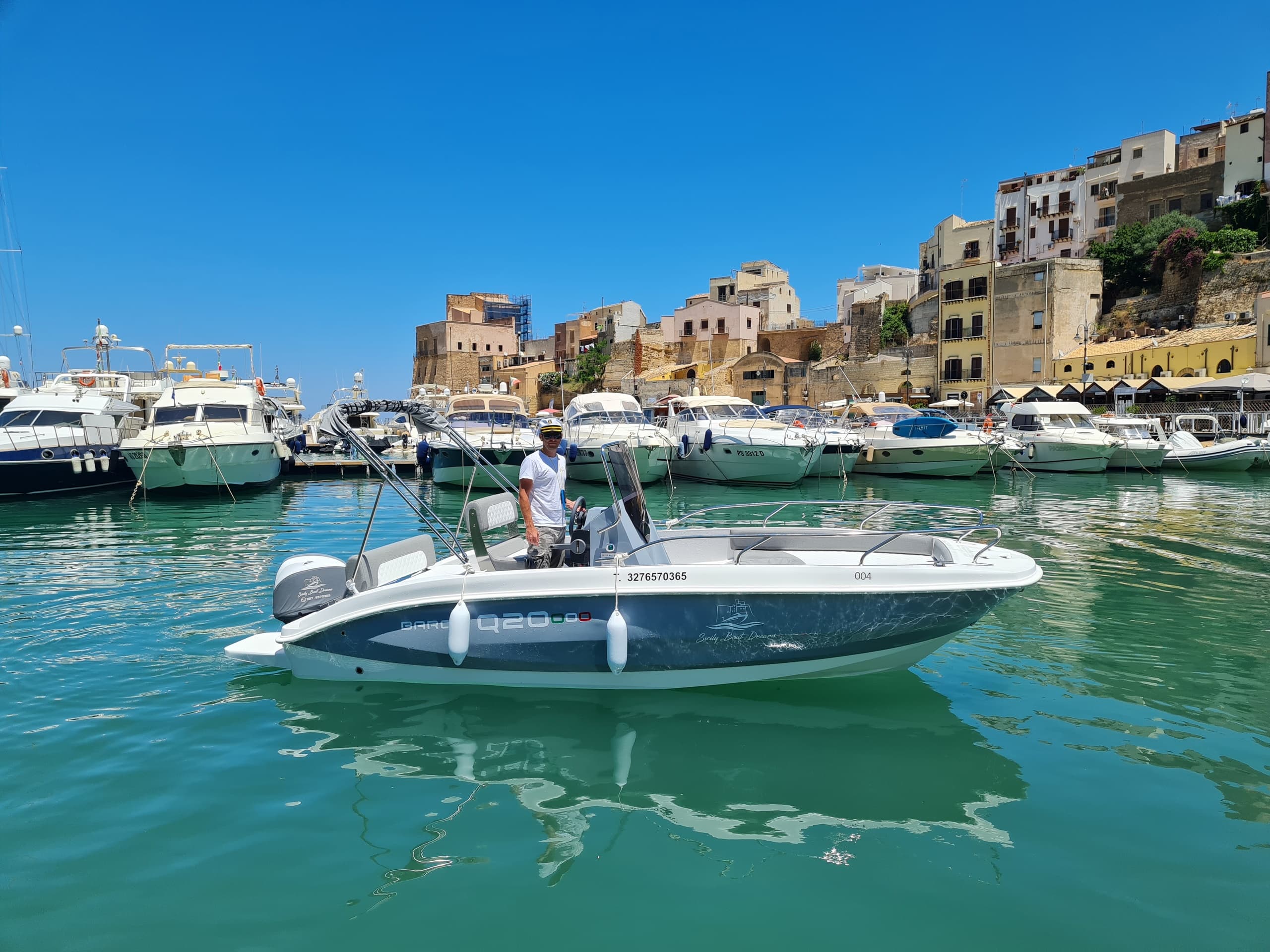 Motorboat in Sicilian harbor with coastal town and clear skies