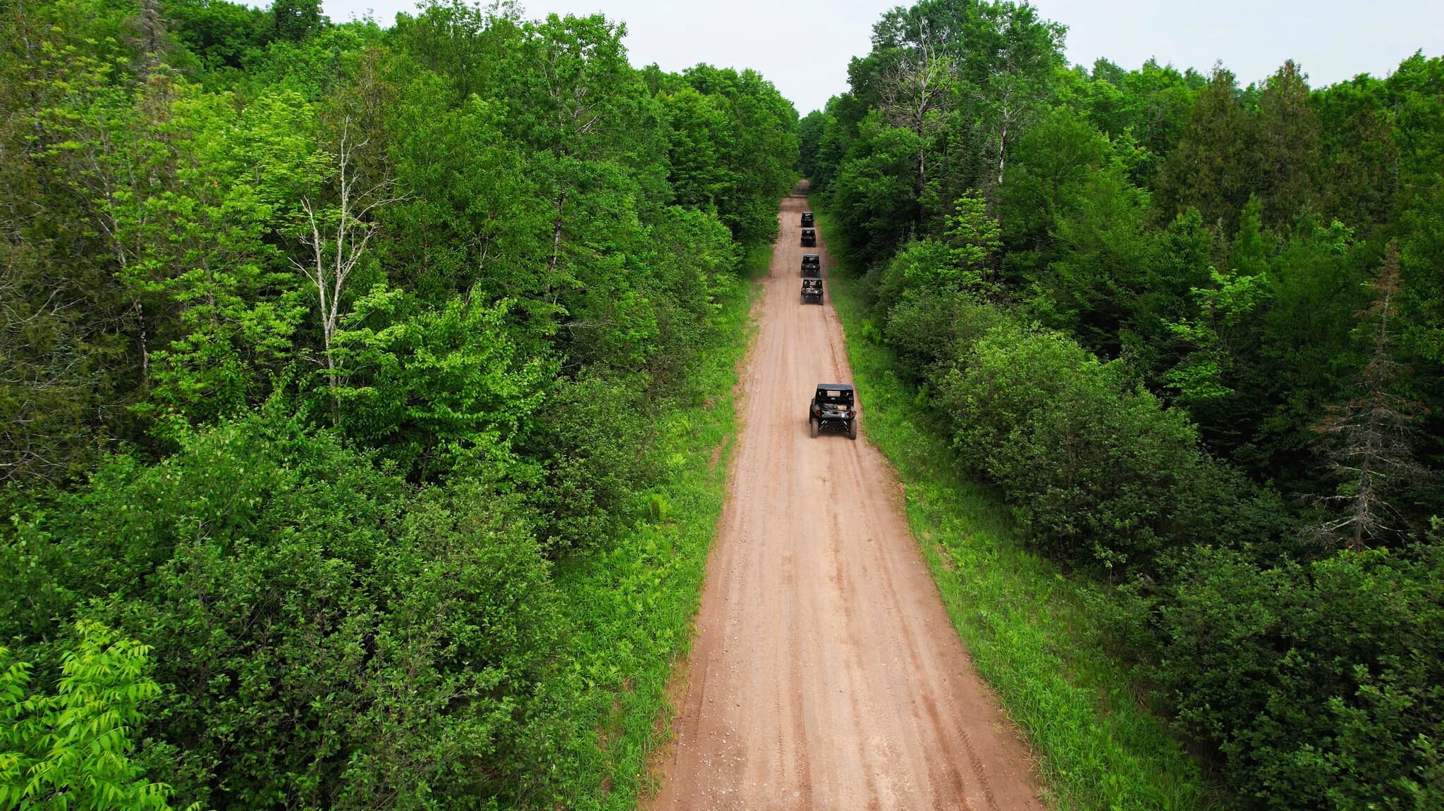 Aerial view of UTV convoy on winding forest road, scenic tour