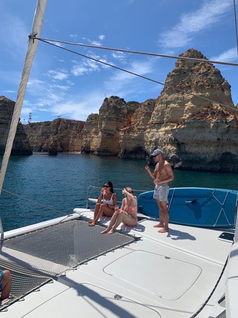 Group relaxing on catamaran near rugged sea cliffs at Algarve