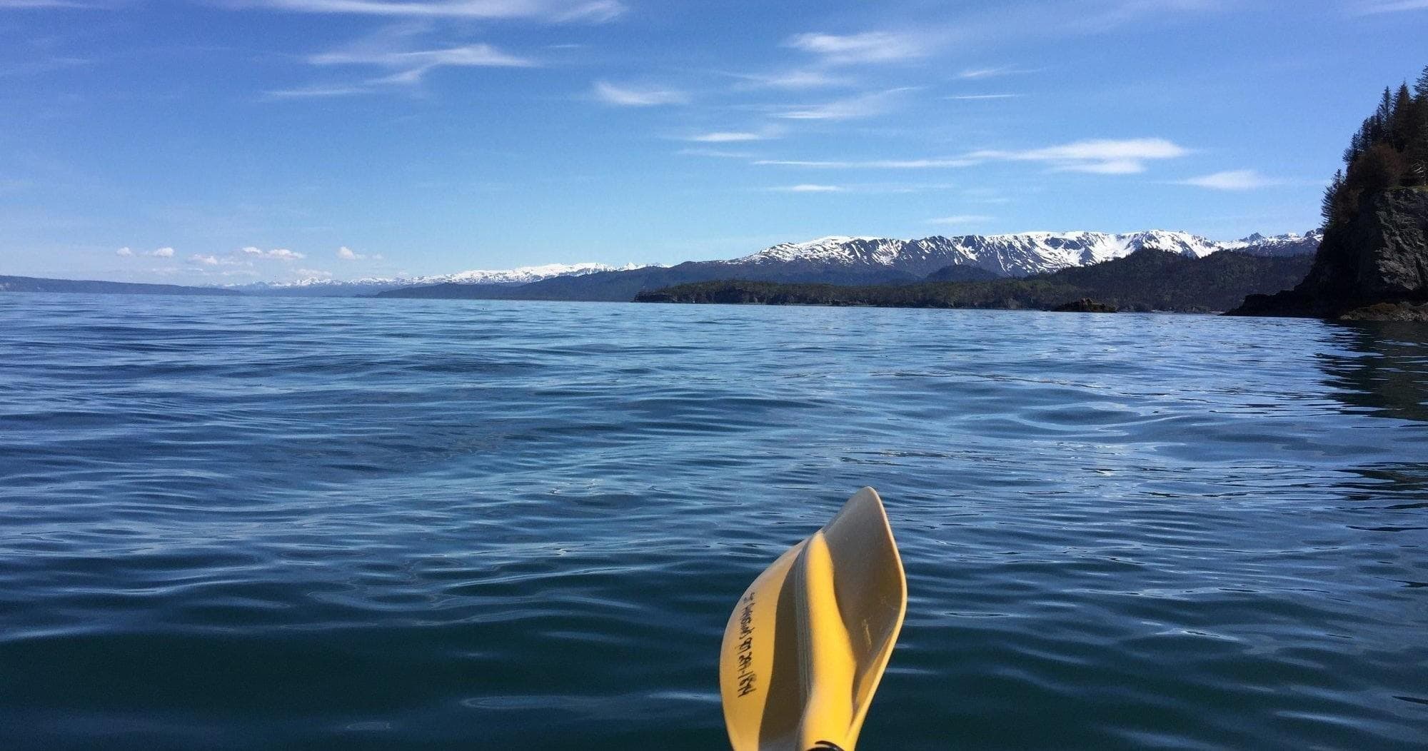 Paddling ocean waters with yellow kayak paddle and coastal mountains