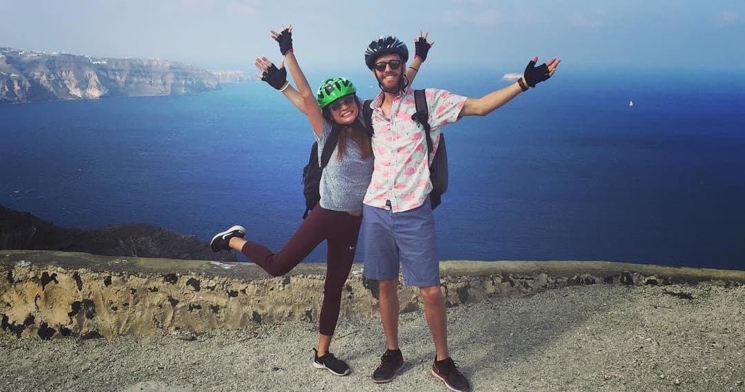Couple jumping with e-bike helmets on Santorini coastal overlook