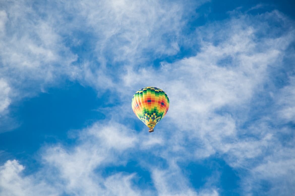 Hot air balloon ride drifting above cloud-filled blue sky
