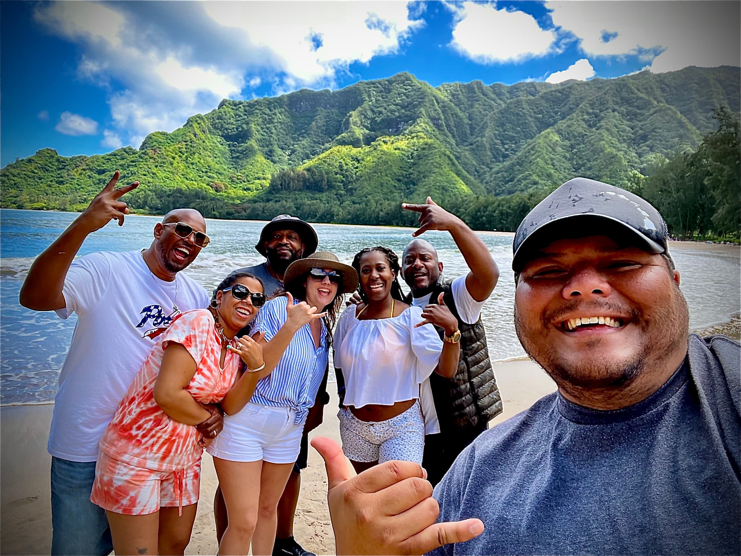 Group selfie on tropical beach with lush Hawaiian mountains