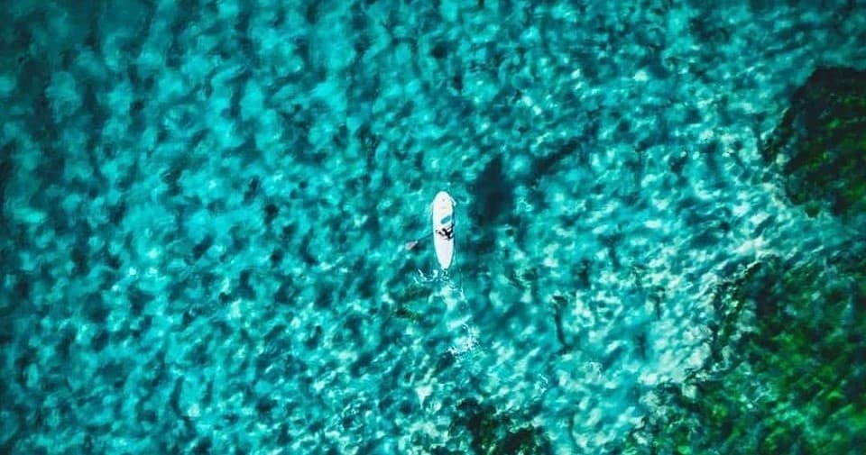 Aerial paddleboarder over turquoise coral reef, tropical ocean