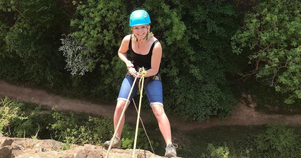 Woman abseiling down limestone cliff into a wooded valley