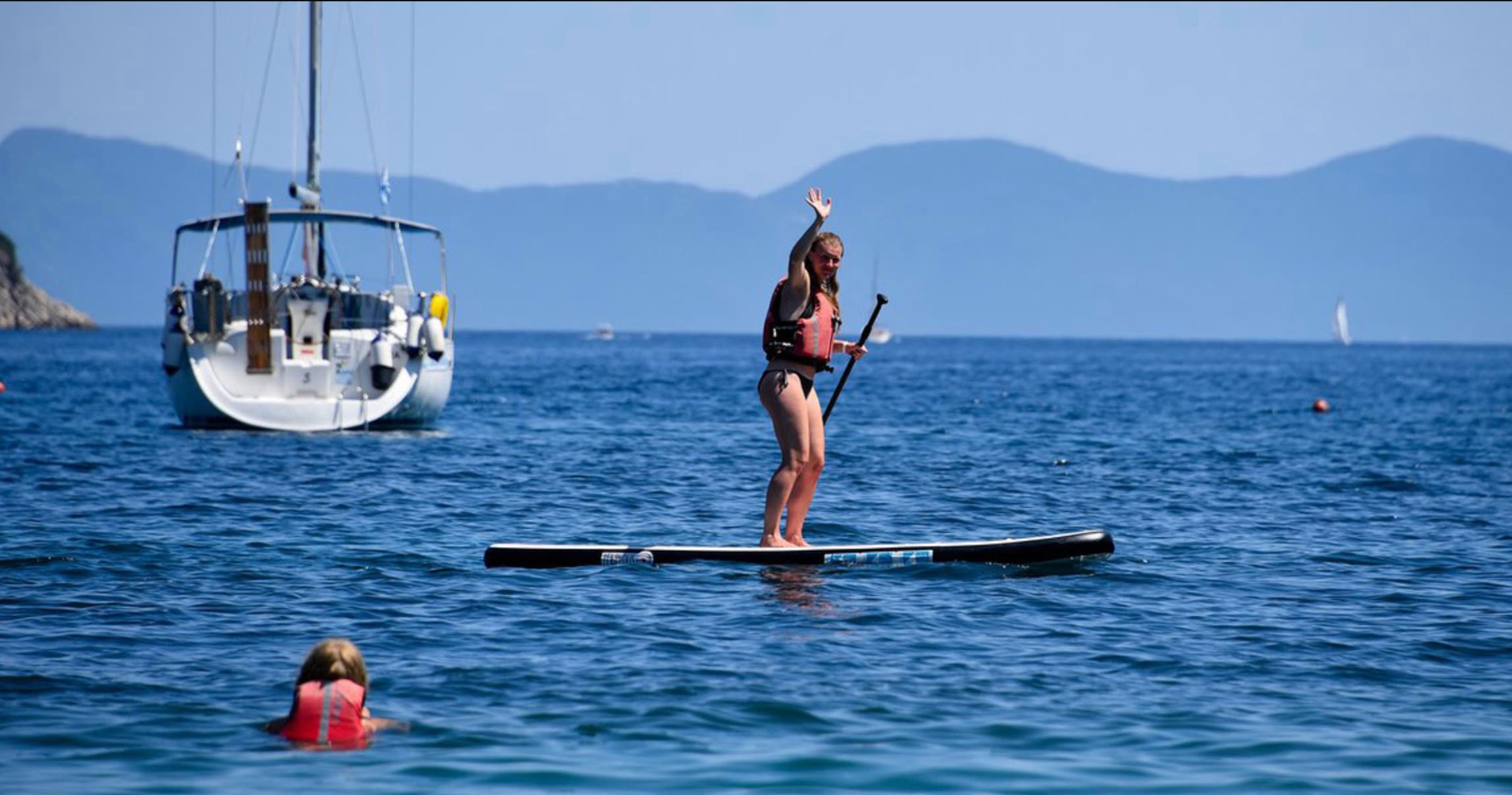 Stand-up paddleboarder near anchored sailboat on open sea