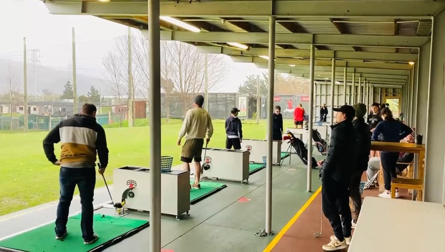 Golfers practicing at covered outdoor driving range bays at club