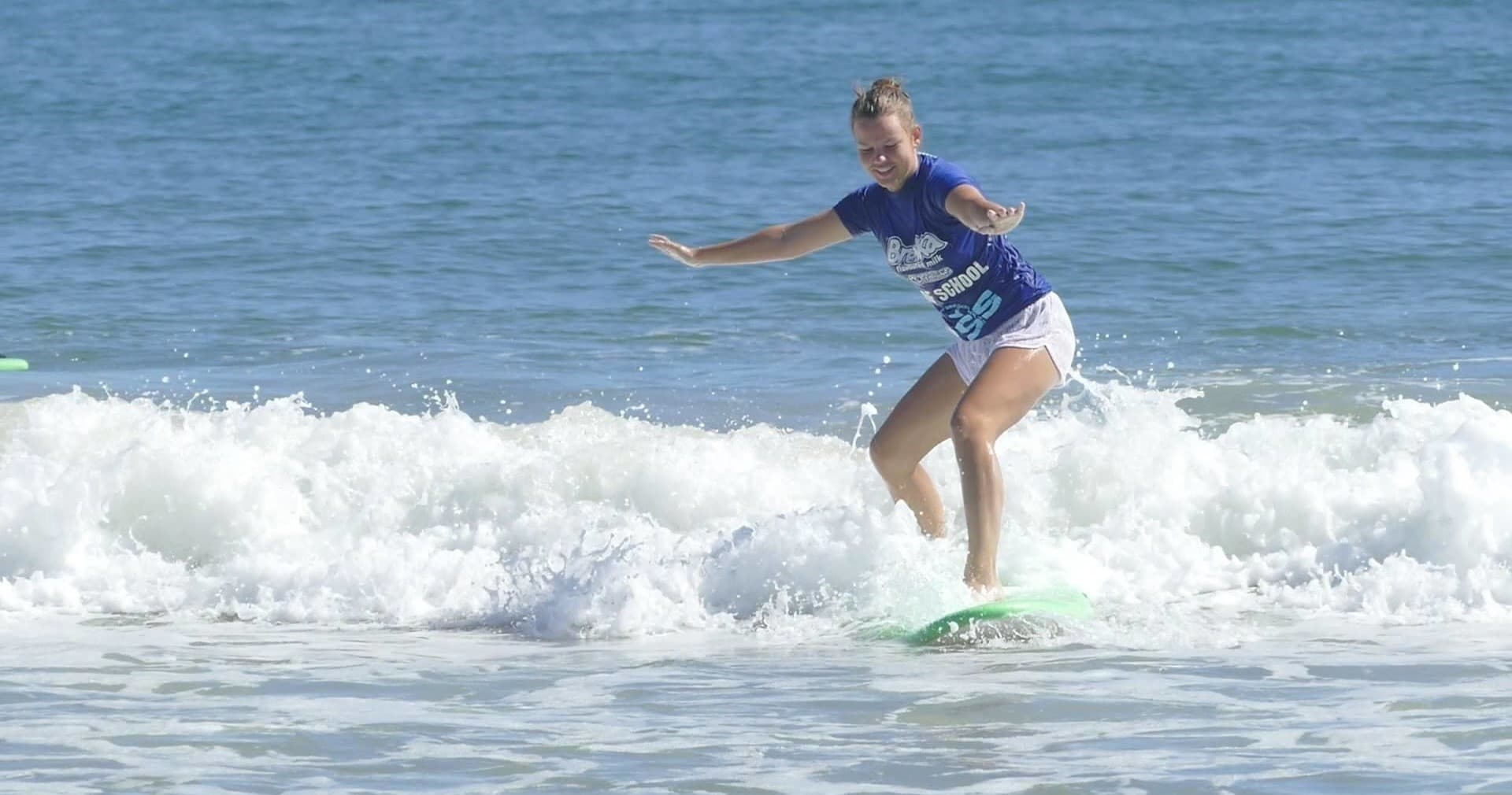 Surfer riding a small breaking wave at sandy beach coast