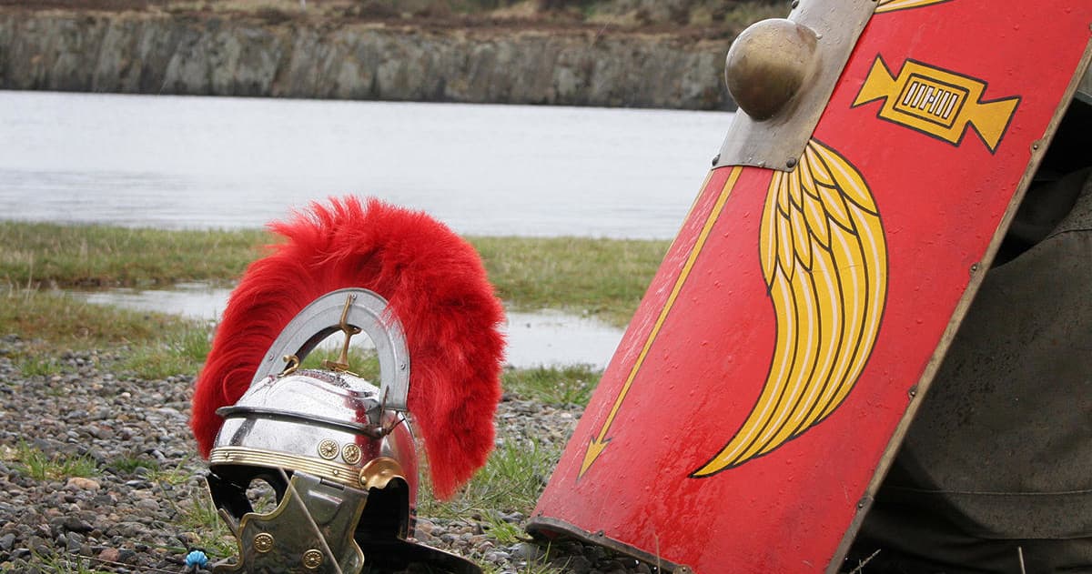 Roman helmet and red shield laid on shoreline at historic site