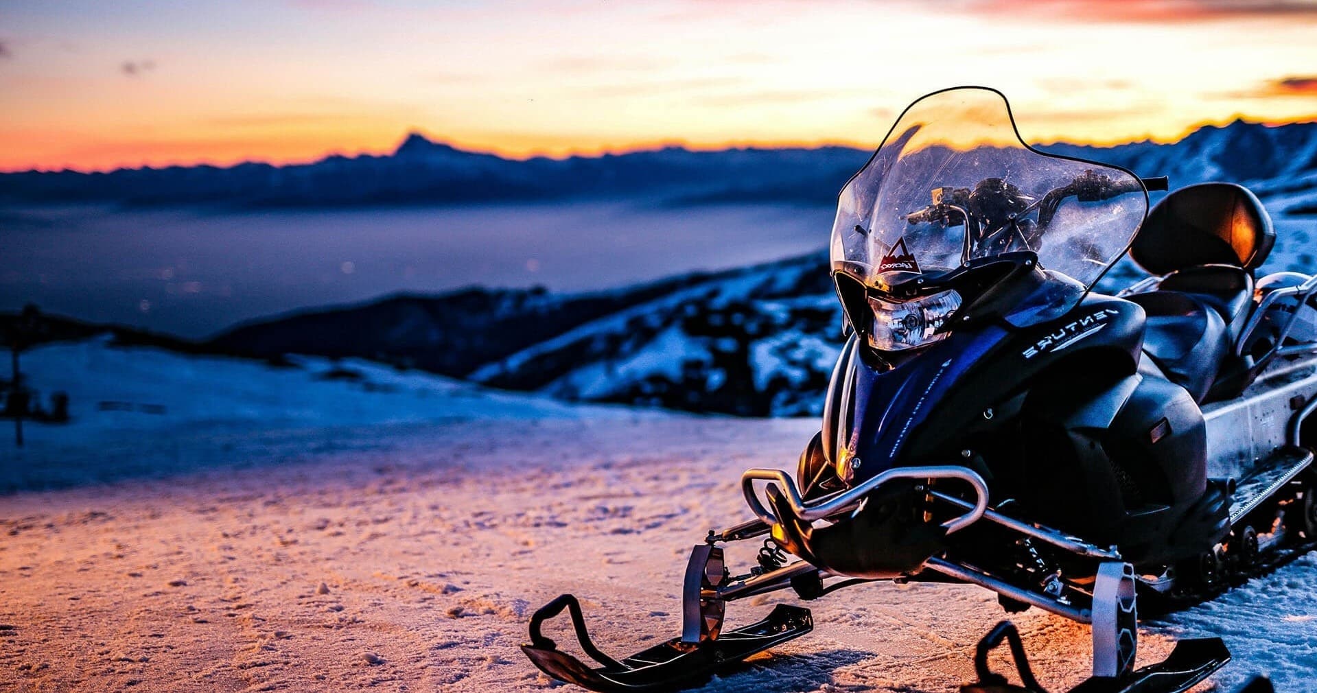 Snowmobile on snowy alpine ridge at sunset showcasing winter ride