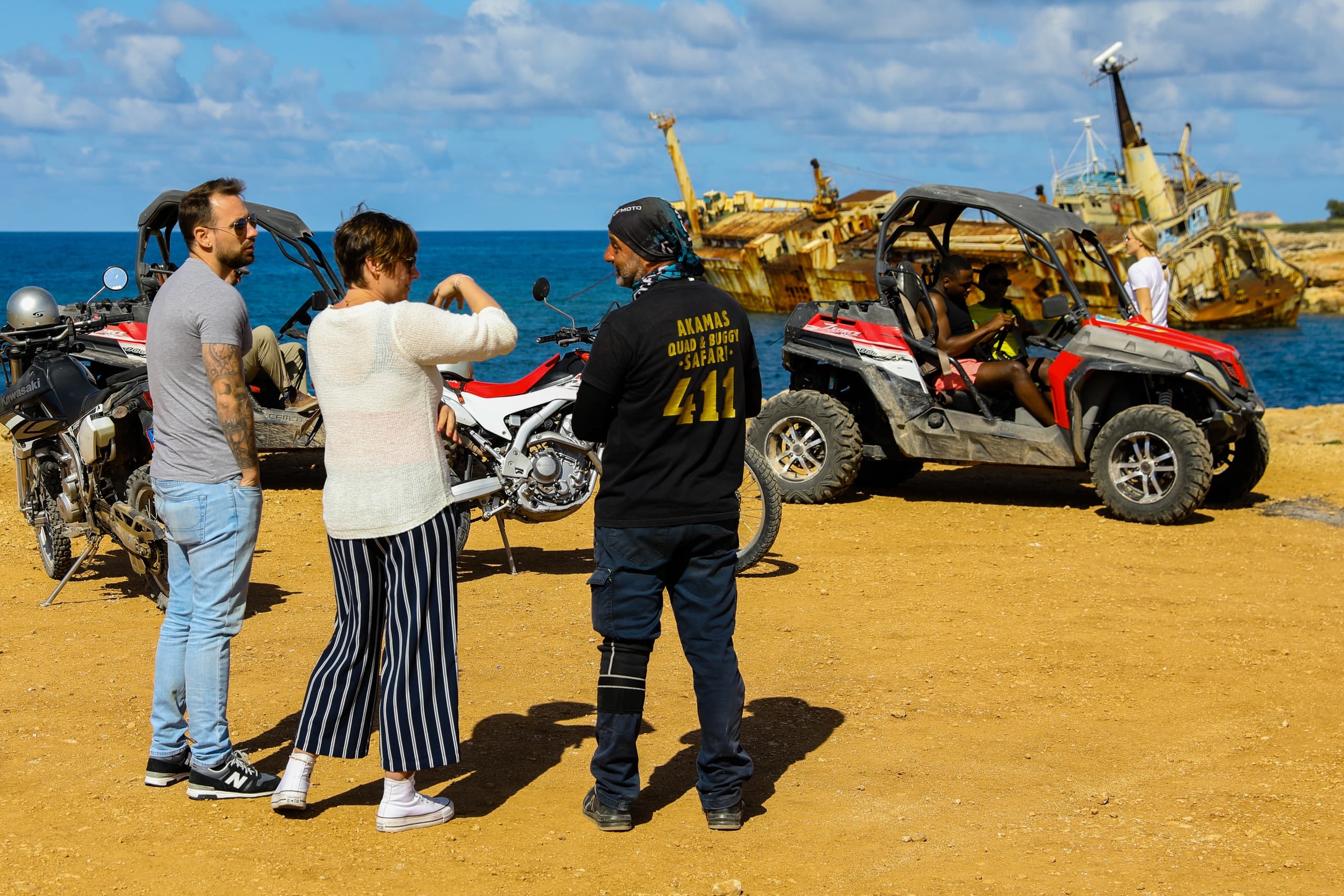 Tourists beside UTVs on golden beach near shipwreck