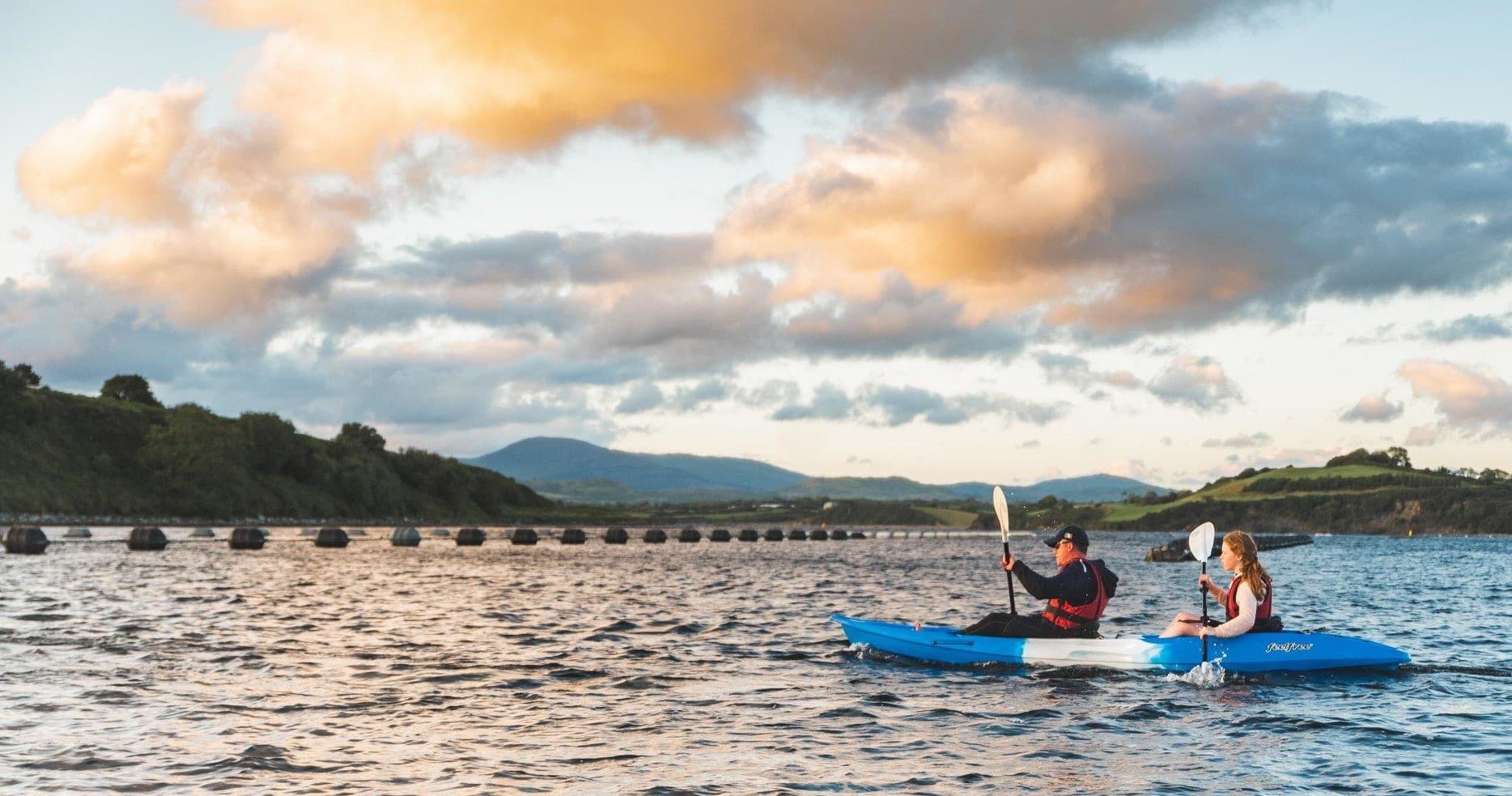 Two kayakers paddling near shore beneath dramatic cloudscape