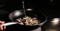 Chef sautéing mushrooms in hot pan in professional kitchen