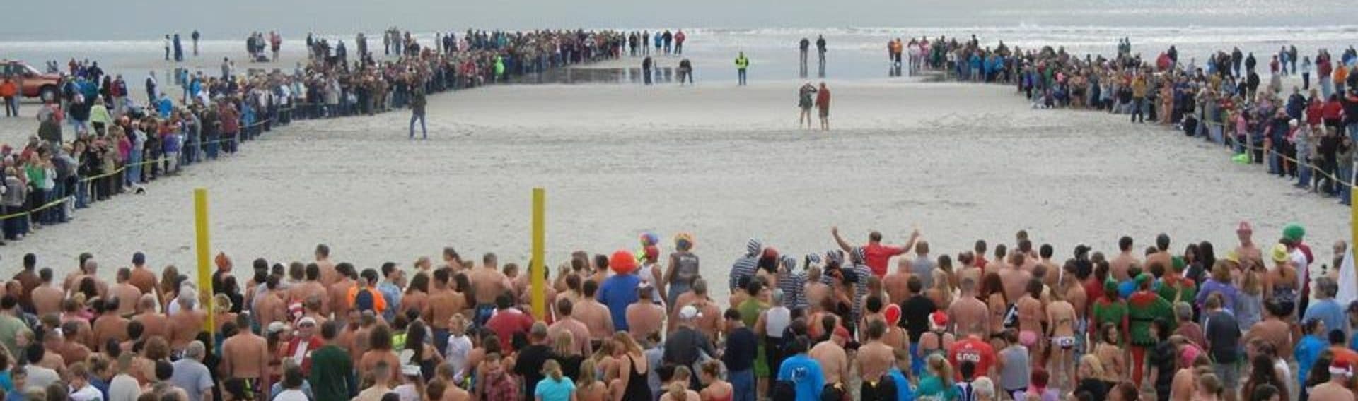 Mass beach plunge with participants running into cold ocean