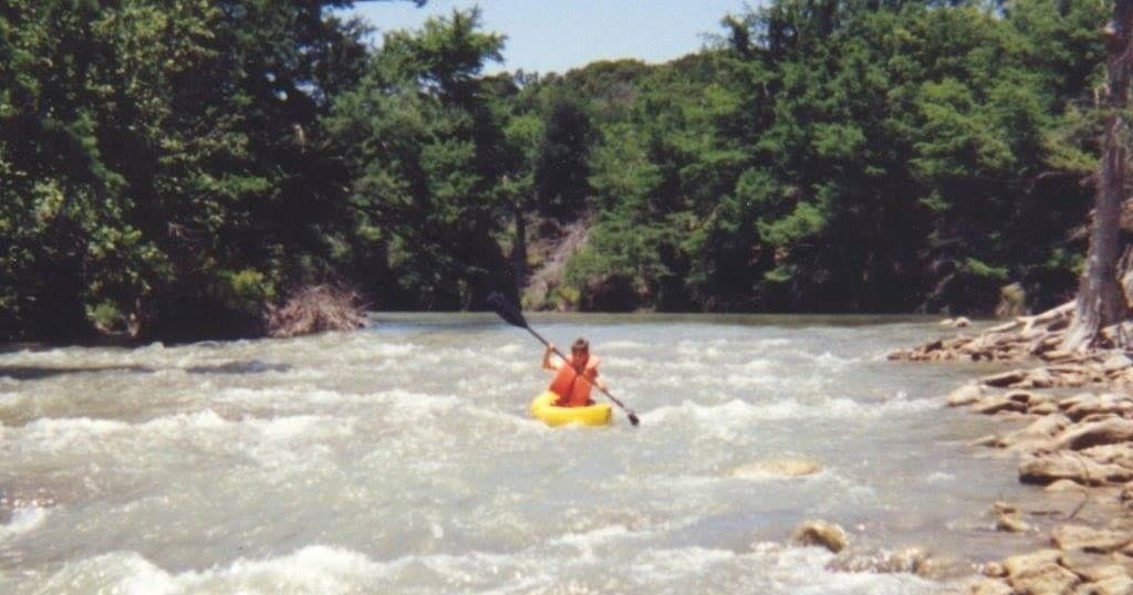 Kayaker navigating whitewater rapids on scenic forested river