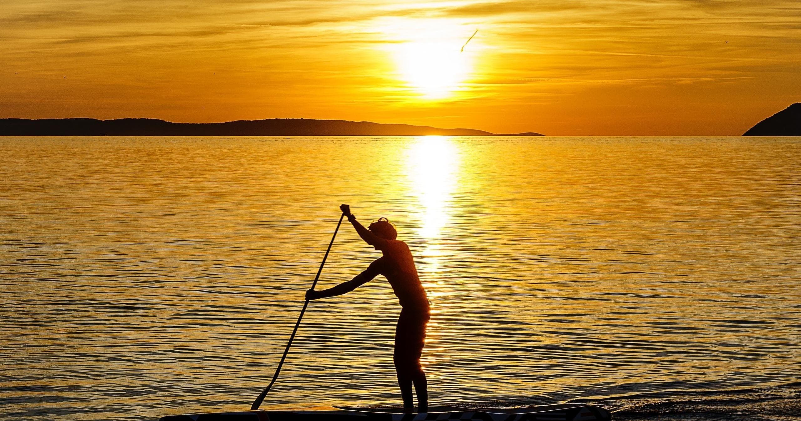 Stand-up paddleboarder silhouetted at sunset on calm sea