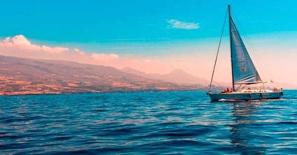Single sailboat on vibrant blue water with distant coastal vista