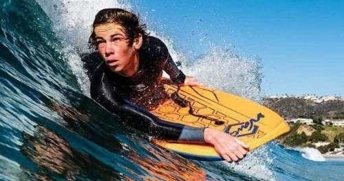 Bodyboarder riding a breaking wave along sunny coastline