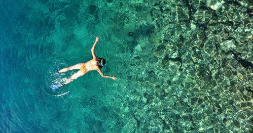 Snorkeler swimming over clear coral reef in Hawaiian waters