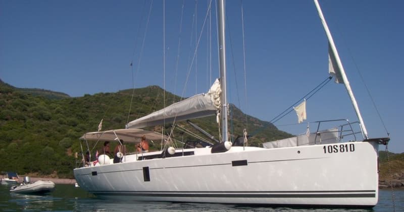 Sailboat anchored near green coastal hills, day charter