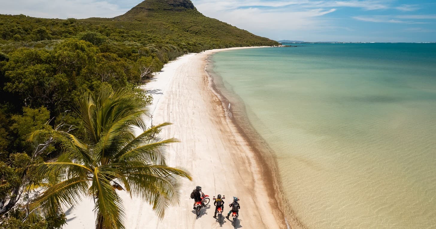 Motorcyclists riding along remote tropical beach at Cape York