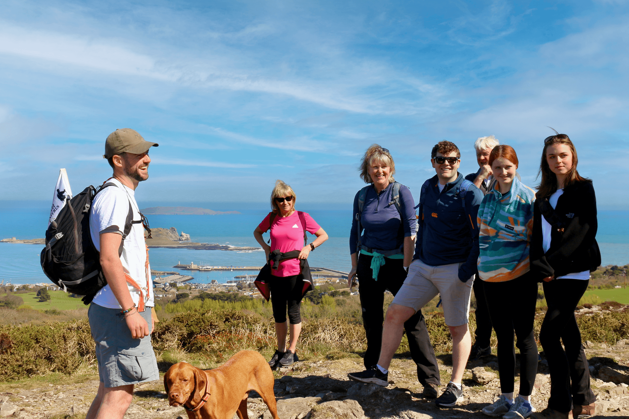 Group coastal walk with dog on rocky shore near blue sea