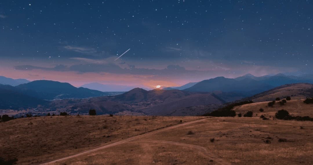 Starry night sky above rolling hills and silhouetted peaks