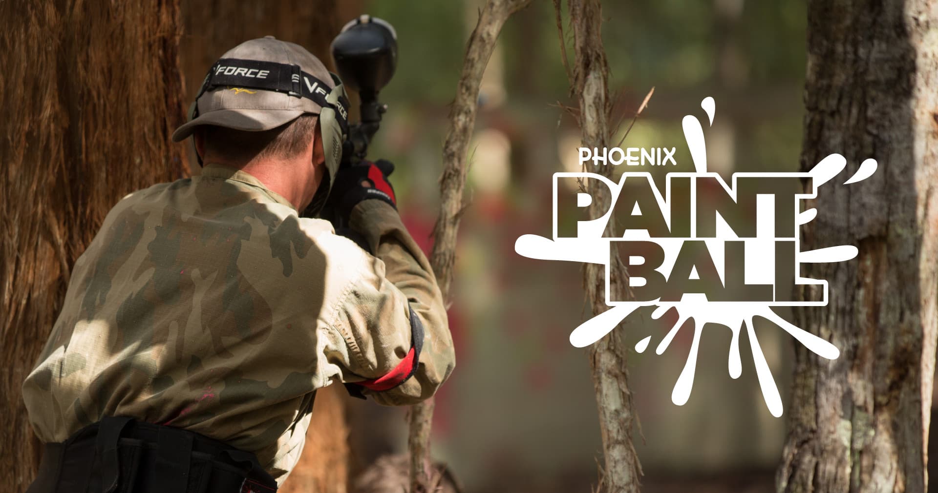 Close-up paintball shooter behind tree on outdoor woodland course