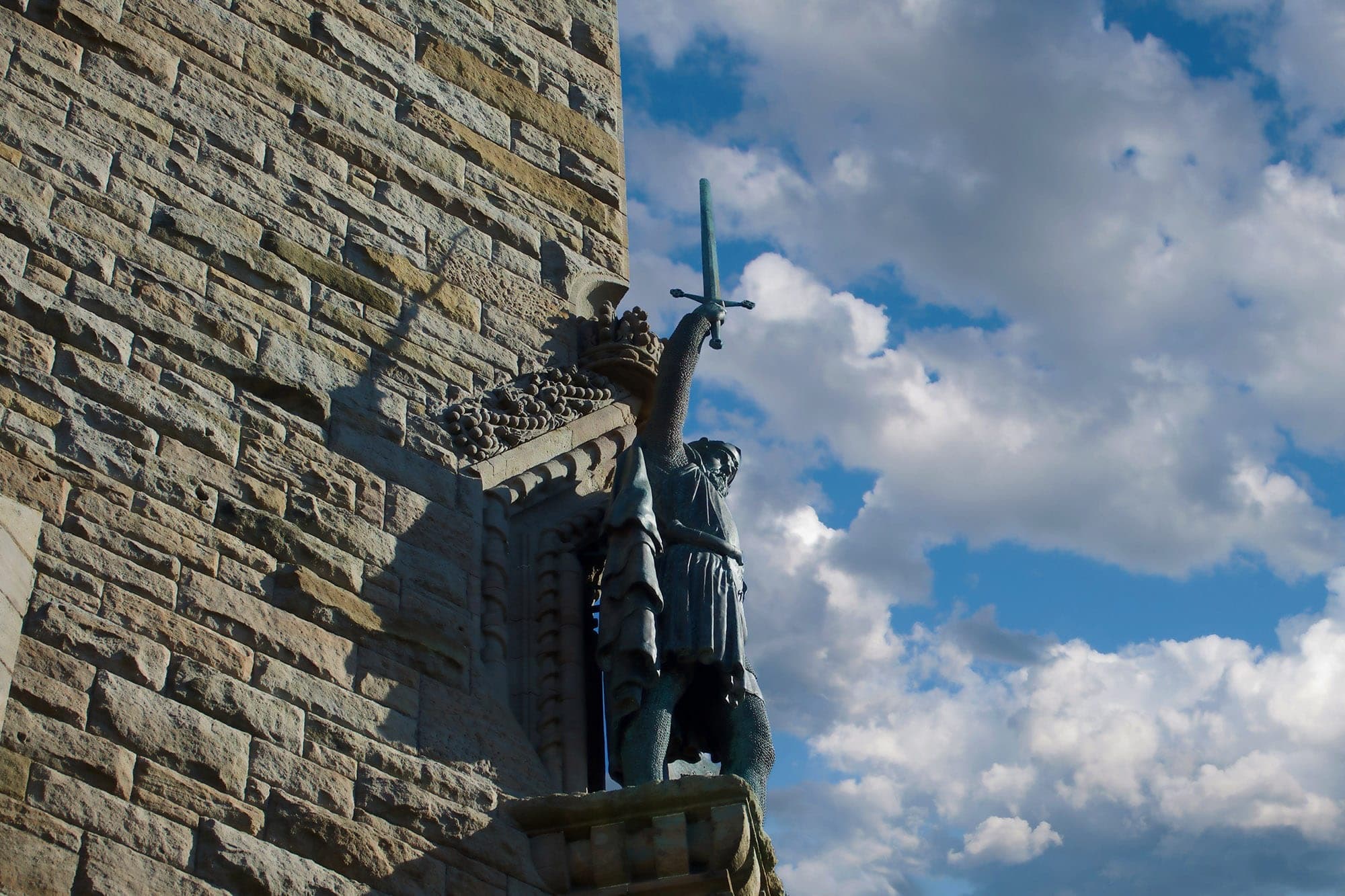 Medieval statue on castle wall under blue sky, historic walking stops