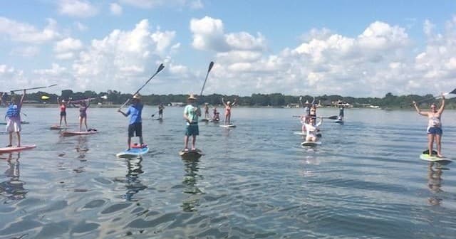 Group paddleboarding on calm lake under blue sky