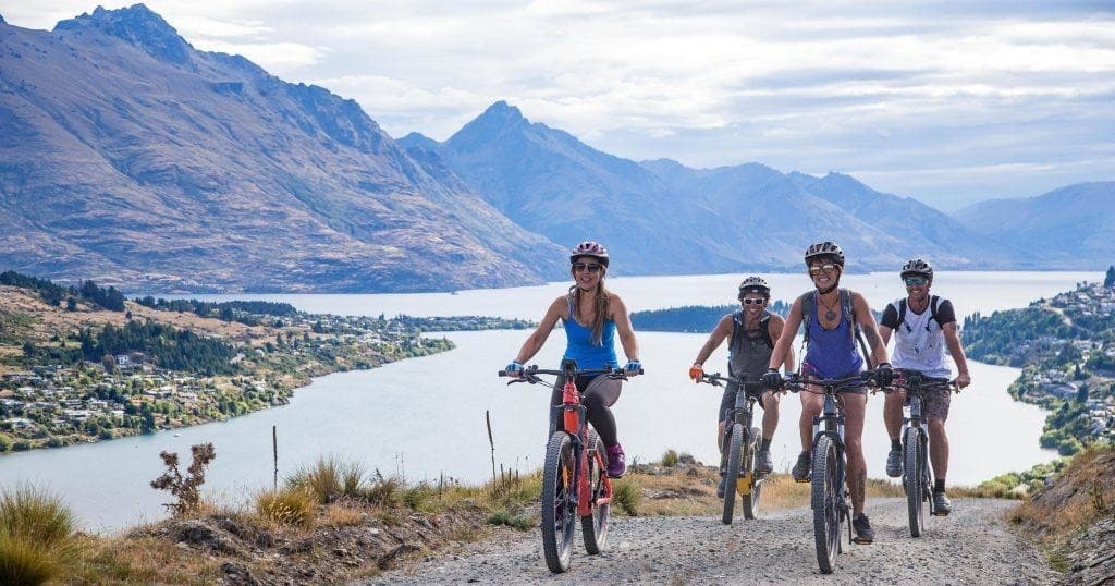 Mountain bikers riding ridge above lake and alpine town