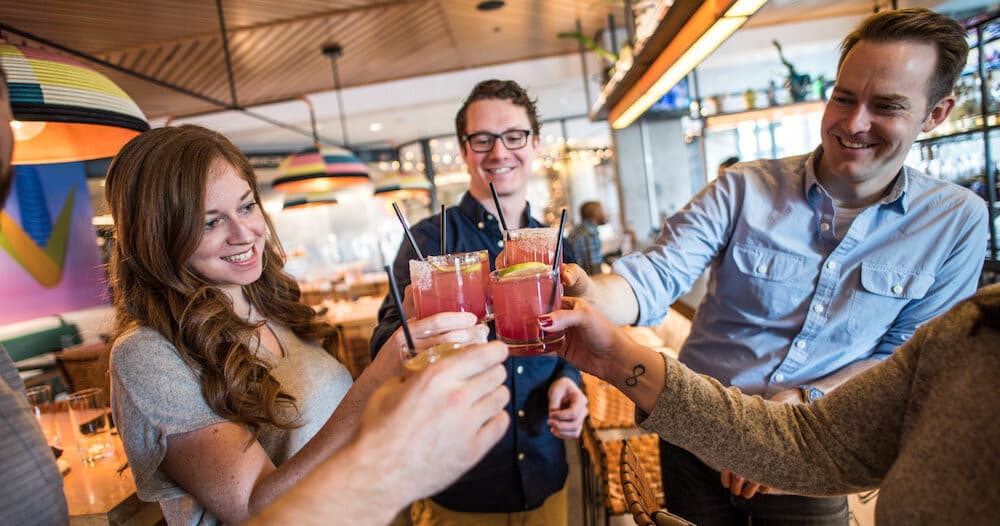 Friends clinking cocktails at lively indoor Denver tavern