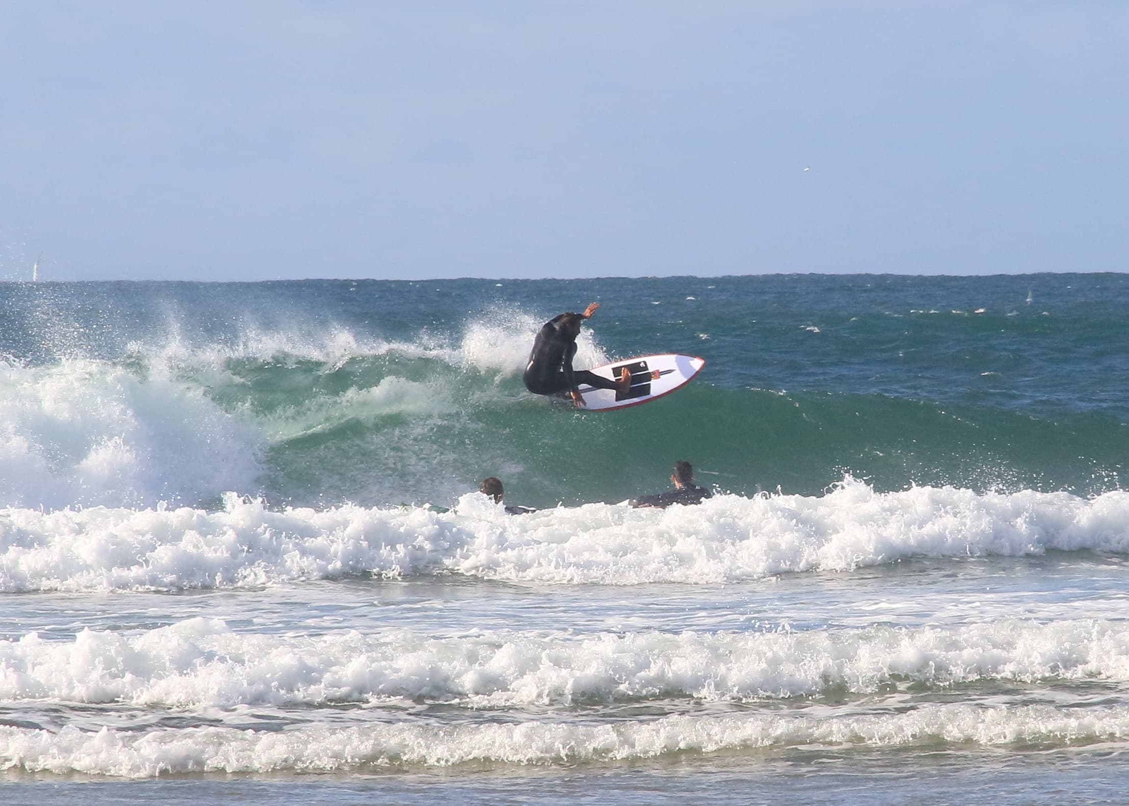 Surfer launching off a wave on open ocean near sandy beach